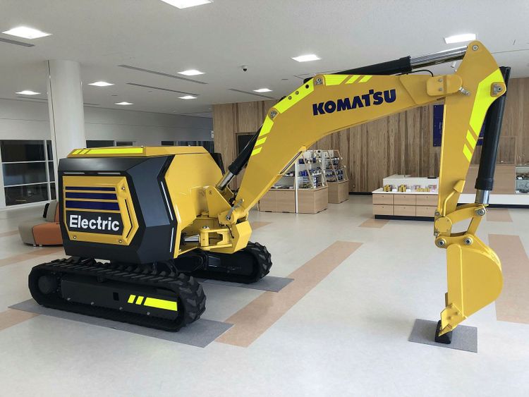 En gul grävare från Komatsu står i en vit utställningshall.