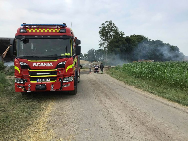 Brandbil på plats vid ladan som brunnit. Rök tornar upp från platsen.