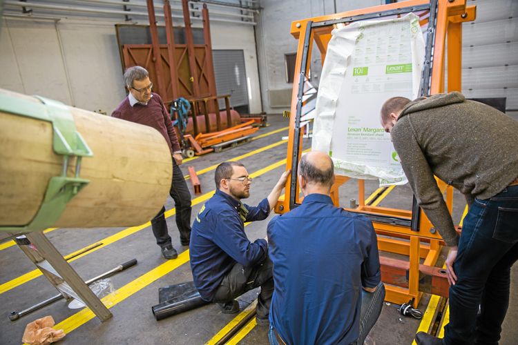 Forskare runt en testrigg för slaghållfasthet hos säkerhetsrutor.