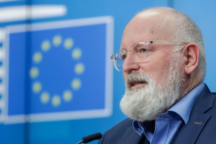 EU-kommissionär Frans Timmermans framför EU-symbol på en presskonferens.