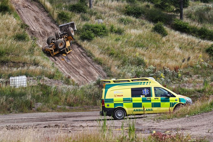 En ambulans står framför en lastmaskin som ligger upp och ner i en slänt.