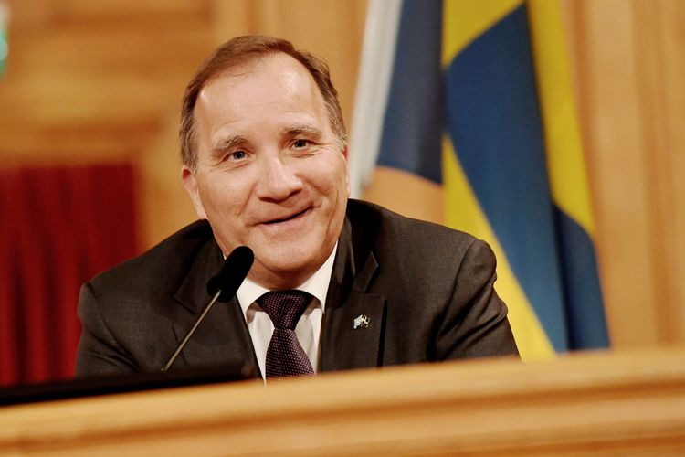 En leende Stefan Löfven sitter framför en mikrofon i riksdagen.